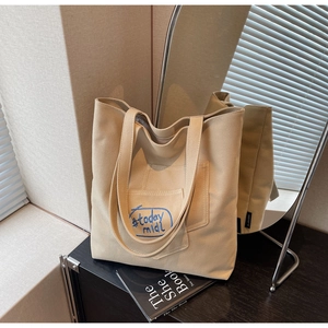 Detail of canvas tote bag featuring embroidered blue text and functional front pocket