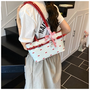 Détail du sac cabas blanc avec imprimés nœuds rouges et pendentif cœur en métal