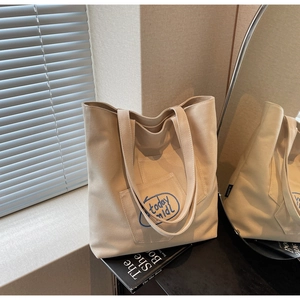 Close-up of beige canvas tote bag with blue 'today midi' embroidery detail and front pocket