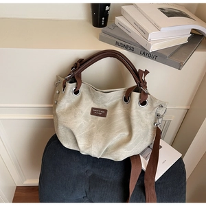 Dettaglio della borsa a mano plissettata beige con manici marroni e patch logo rettangolare