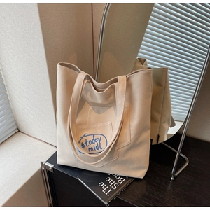 Detail of beige canvas tote bag showing front pocket with blue #today midi embroidery