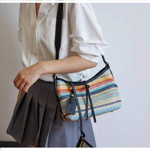Detail of hand-woven colorful striped straw bag with black leather shoulder strap and hardware