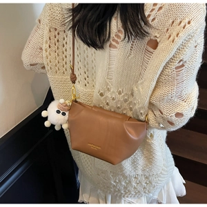 Sac bandoulière en cuir marron avec charme en peluche blanche porté par un mannequin