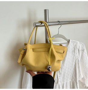 Detail of yellow pebbled leather bucket bag with silver heart charm and ruffled texture