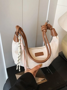 Chic cream dumpling bag with brown leather knotted handles and colorful braided pendants
