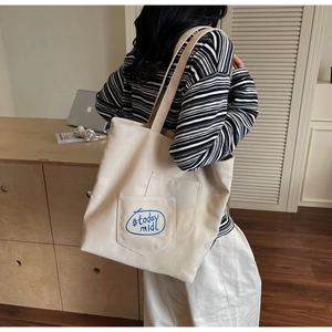 Detail showing the cream canvas tote bag side view with blue embroidery and outer pocket