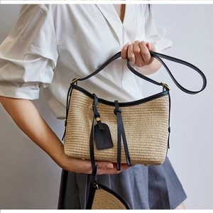 Detail of woven straw handbag featuring black leather trim and metallic bottom studs
