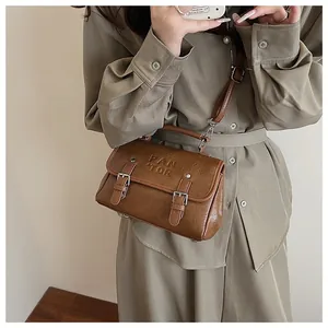 Close-up of a vintage brown leather crossbody bag with silver buckles and embossed text