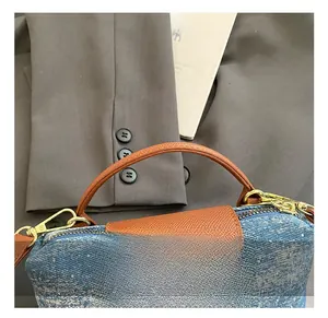 Detail of denim and brown leather stitching on a small square crossbody shoulder bag