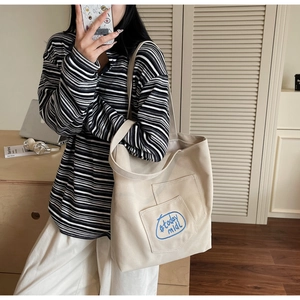 Mirror selfie showing the large beige canvas tote bag with front pocket and blue embroidery