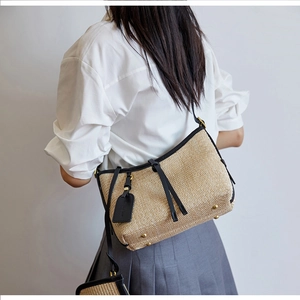 Detail view of woven straw crossbody bag featuring black leather straps and gold metal feet