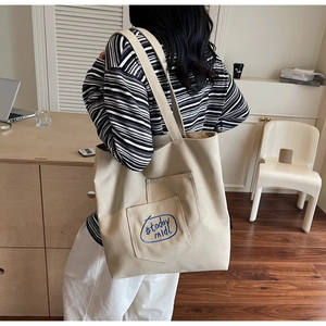 Close-up of beige canvas tote bag with blue 'today midi' lettering and wide shoulder strap