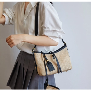Detail of woven straw shoulder bag with black leather trim and fashion tag on white dress