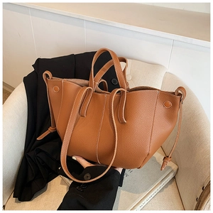 Detail of a brown lychee pattern leather tote bag with expandable wings on a soft sofa