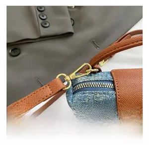 Detail of light gold alloy hook and zipper on denim small crossbody bag with leather strap