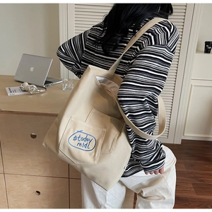 Detail of beige canvas tote bag showing front pocket with blue letter embroidery