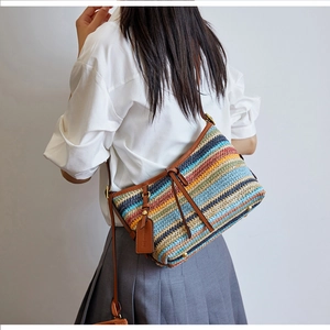 Detail of multi-color striped straw bag with leather trim and metal feet on the bottom