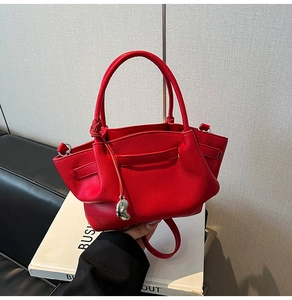 Detail of red pebbled leather winged bucket bag featuring a silver heart charm
