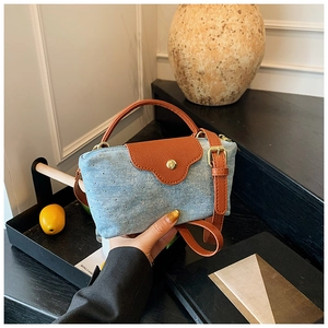 Detail of denim crossbody bag with orange leather trim and silver stud accents