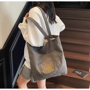 Detail of deep grey canvas tote bag featuring yellow #today midi embroidery on pocket