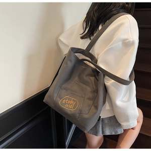 Detail of grey canvas tote bag with yellow embroidery on an outdoor wooden staircase