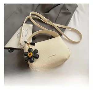 Detail of beige litchi grain leather bag with a sunflower charm on a grey trench coat