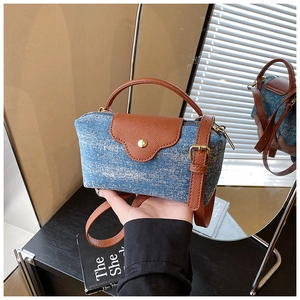 Detail of blue denim and brown leather crossbody bag with metal buckle and handle