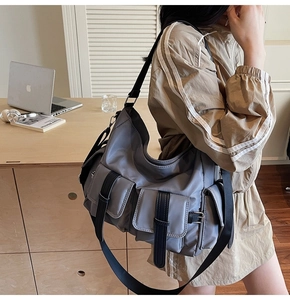 Detail of grey utility tote bag with buckle pockets and wide black strap on shoulder