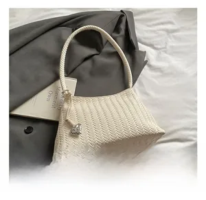 Detail of cream woven shoulder bag featuring intricate texture and a heart charm