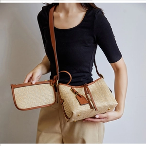 Detailed view of straw woven shoulder bag with brown leather trim and small pouch charm