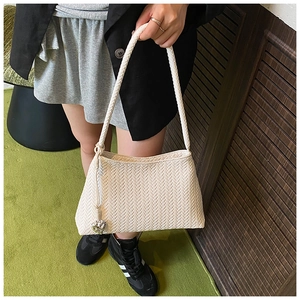 Detail of cream woven shoulder bag with intricate texture and silver heart pendant charm