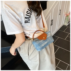 Detailed view of light blue denim crossbody bag with brown leather strap worn by a model