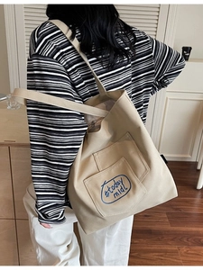 Minimalist canvas tote bag in beige with blue embroidery shown on a female model