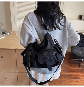 Rear view of model wearing a black nylon multi-pocket utility tote bag with metal buckles