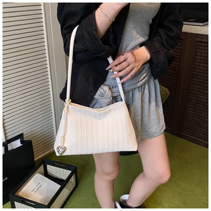 Detailed view of white woven shoulder bag with silver heart charm and V-stitch pattern