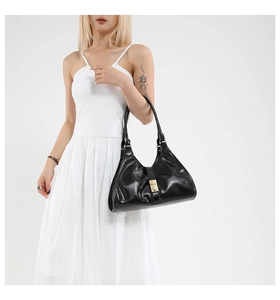 Détail d'un sac bandoulière noir brillant avec un fermoir métallique doré carré