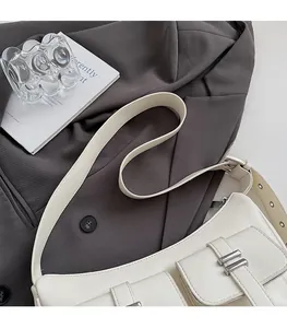Close-up of cream leather shoulder bag with decorative silver buckles and wide strap