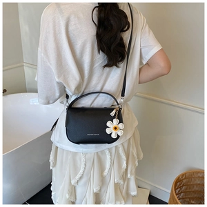 Detail of black lychee texture leather handbag with daisy charm and fashion text print