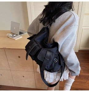 Detail of black multi-pocket crossbody tote bag with adjustable strap in a workspace setting