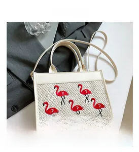 Détail de broderie flamant rose sur sac cabas tissé blanc avec lanières en cuir