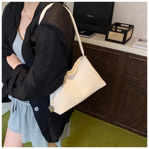 Close-up of cream woven shoulder bag featuring a silver heart-shaped zipper charm