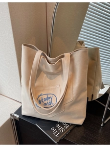 Minimalist off-white canvas tote bag with blue embroidery on dark wood table