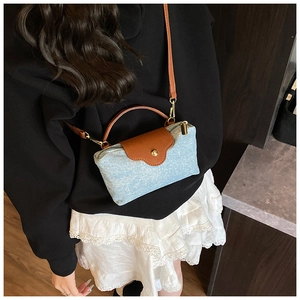 Detail view of light blue denim crossbody bag with brown leather trim worn by a model