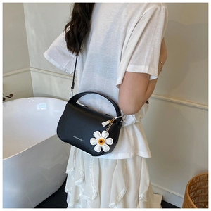 Detail of black lychee texture bag with daisy charm worn crossbody by a model