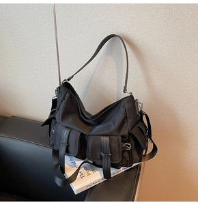 Detail shot of a black multi-pocket nylon tote bag with utility buckles on a sofa