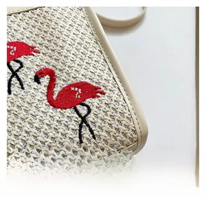 Gros plan d'un sac en paille tissé avec broderie flamant rouge et détails en cuir