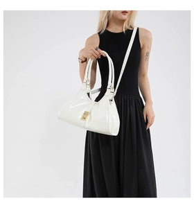 Détail du sac bandoulière en cuir verni blanc avec boucle dorée porté par un mannequin