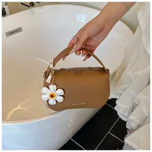 Close-up of brown litchi pattern leather handbag with a white daisy floral charm