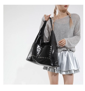 Detail of glossy black faux leather tote bag with silver hexagonal metal rivets