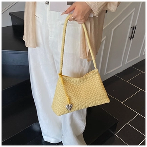 Detail of yellow woven bucket bag with elegant herringbone texture and heart-shaped pendant